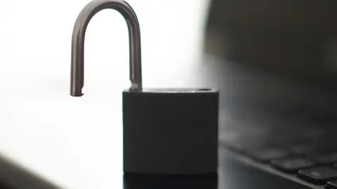 Lukket bærbar PC ved siden av en hengelås som ligger på en haug med sjetonger på et mørkt skrivebord